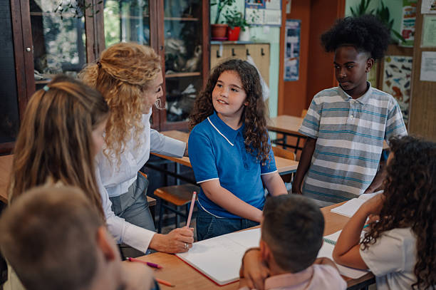 istock Teacher helping young girl student during class in elementary school 2218662903