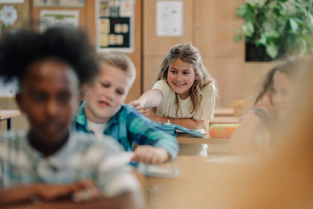 istock Smiling schoolgirl reaching out to classmate in elementary school classroom 2218663005