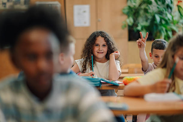 istock Elementary school students raising hand and smiling in classroom 2218663160
