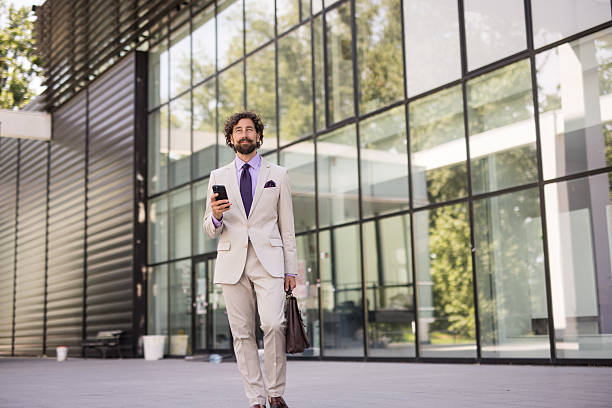 istock Businessman walking and using smartphone in front of modern office building 2218663655