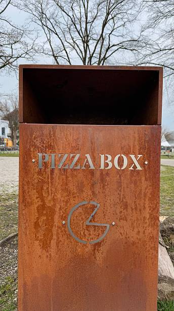 istock Rusty metal pizza box trash receptacle in urban park setting surrounded by trees and grassy area promoting cleanliness 2218670947