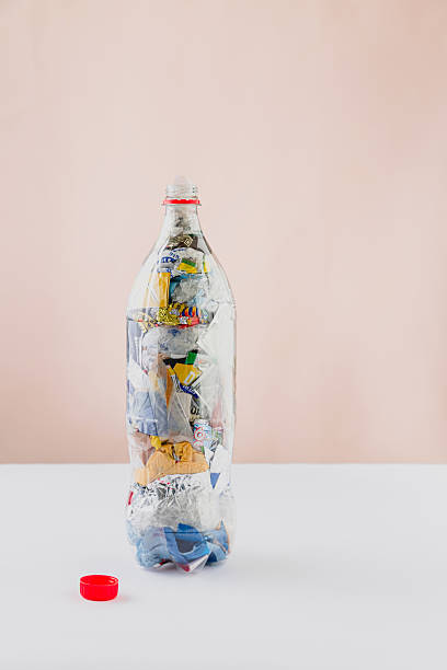 istock lo eco brick PET bottle stuffed with plastic wrappers on white surface and light pink background. Red cap. 2218673093