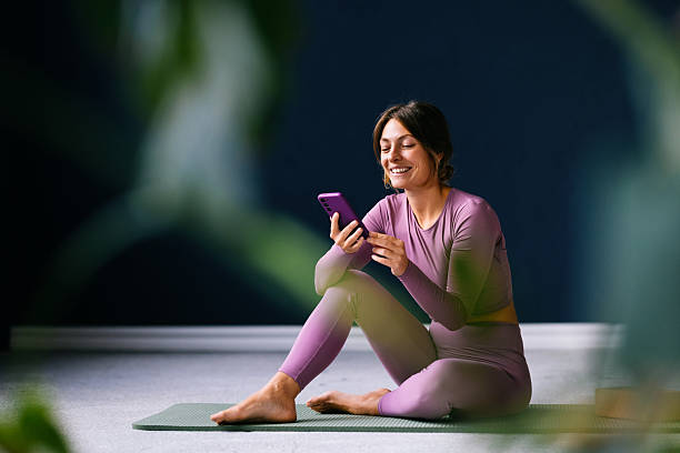 Smiling Woman Relaxing on Yoga Mat While Using Smartphone in Casual Setting
