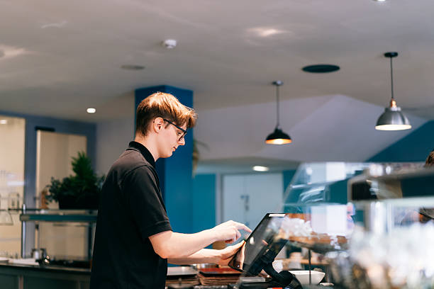 istock Young waiter serving customer at cash point in cafe. Man working with POS terminal. Student working part-time. Problems of unemployment and Job opportunities for youth. Small business vacancies 2218677996