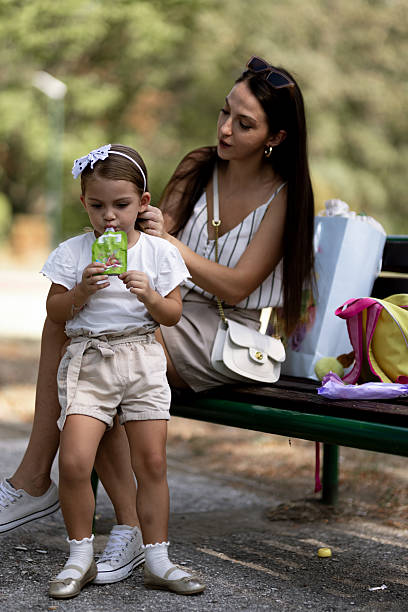 Mother brushing her daughter's hair while sitting on a park bench