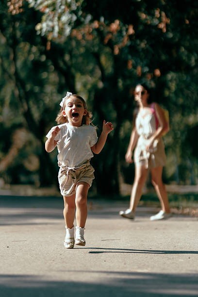 istock A joyful child running outdoors in a park under sunlight with an adult watching from a distance creating a fun and lively moment of carefree play. 2218683207