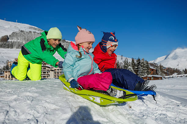 istock Joyful kids slide down a snowy slope in bright winter jackets 2218684507