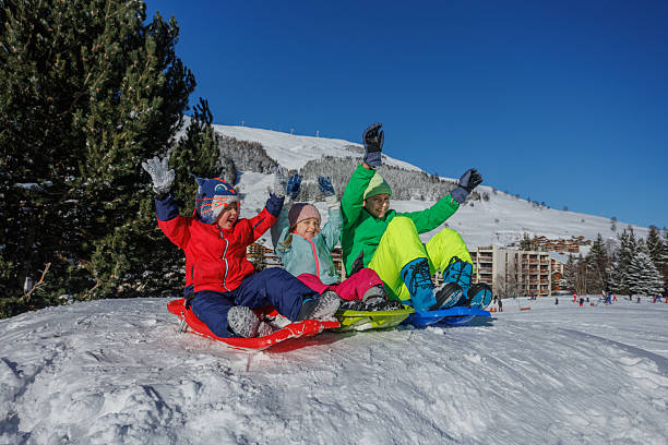 istock Three kids sit on sled arms raised against mountain backdrop 2218684508