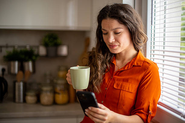 istock Woman drinking coffee and reading messages on smartphone in kitchen 2218684855