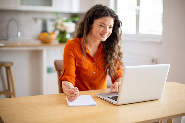 istock Young woman working from home taking notes while looking at laptop 2218685202