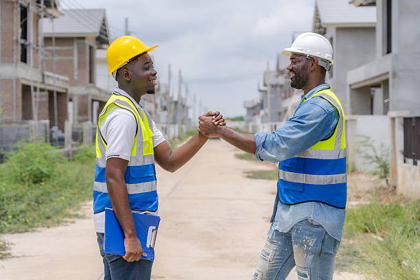 istock Engineer and worker wearing hard hats and reflective vests hold hands outdoors, emphasizing successful teamwork and cooperation on construction projects. 2218696564