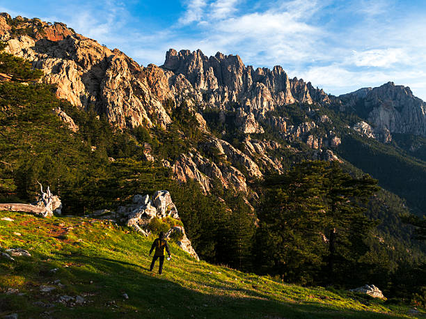 Rear view of a hiker standing in nature enjoying the view of the mountain landscape at sunrise, Aiguilles de Bavella, Corsica, France