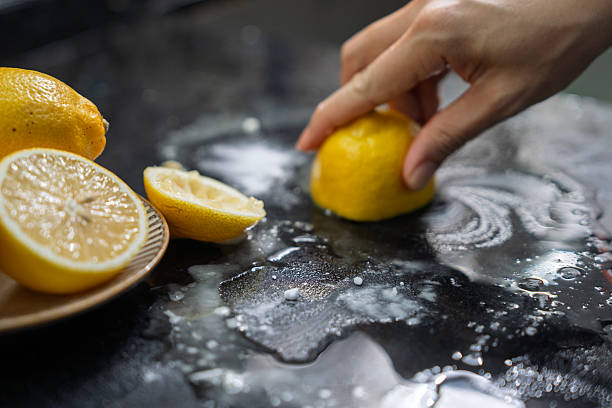 A close-up of a hand scrubbing a black countertop with half a lemon and baking soda, showcasing a natural and eco-friendly household cleaning method.