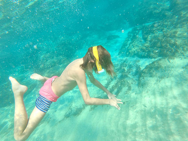 Young caucasian boy moving down underwater. He is swimming and diving in clear turquoise colored sea.