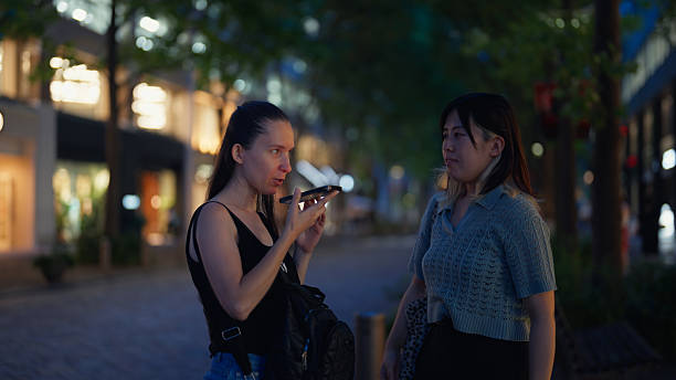 istock Female solo traveler using artificial intelligent mobile app to communicate and ask directions to local person in city street in Tokyo 2218715879
