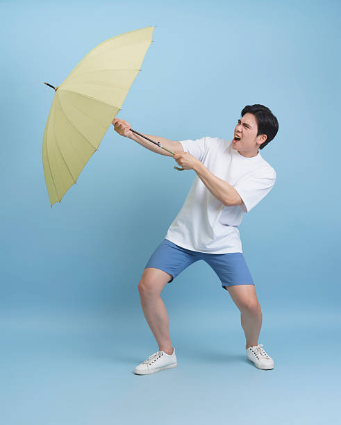 istock Person Struggling with Yellow Umbrella on Blue Studio Background 2218718861