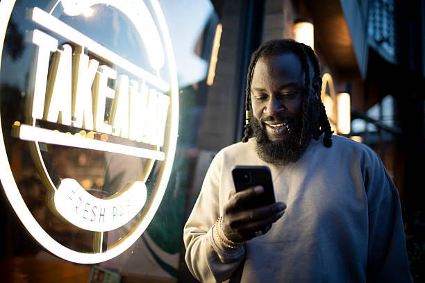istock Man using a smartphone next to an illuminated takeaway food sign at night 2218719144