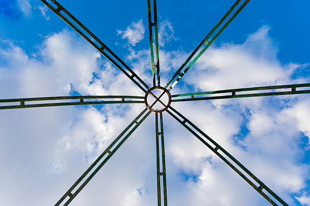 istock Symmetrical green metal structure viewed from below with a circular center, contrasted against a vibrant blue sky with scattered clouds. 2218724248