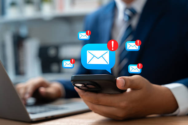 istock Businessman receive multiple scam email alerts on smartphone while multitasking on laptop. Email notifications, malware, Concept of cybersecurity threat, Phishing scam, Email overload in workplace. 2218724676