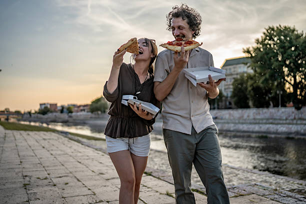 istock Smiling Couple Enjoying Pizza Outdoors by a Scenic River at Sunset 2218725210