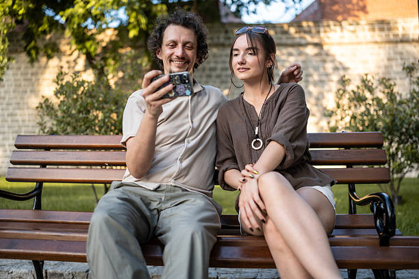 istock Happy Friends Sitting on a Bench and Watching a Phone Together 2218725307