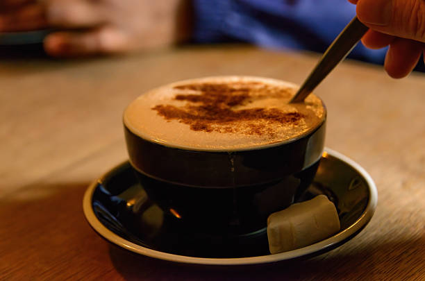 Hand holding a spoon over a cup of coffee.