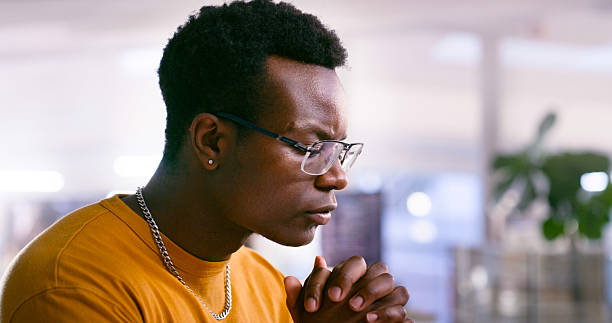 Contemplative Young Man in Office Environment Reflecting with Hands Clasped