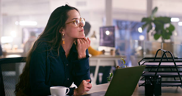 Woman in Office Reflecting While Working Late with Laptop and Coffee
