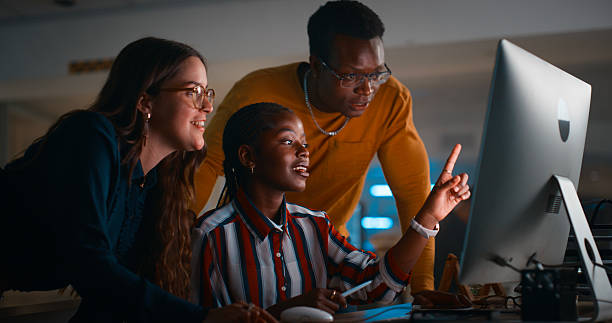 Young Professionals Collaborating on a Computer in a Modern Darkly Lit Office Setting stock photo