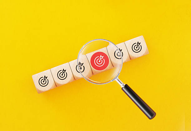 Black magnifying glass on target symbols written cubes over yellow background. Horizontal composition with copy space.