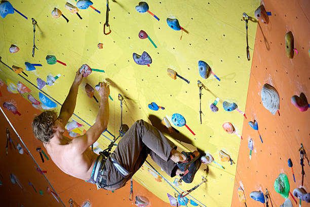 Young male climber athlete with naked torso climbing up on the wall