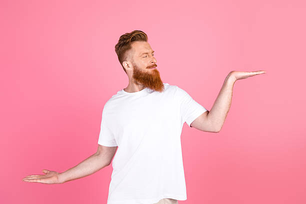 istock Stylish young man showcasing gestures with open hands against a bright pink background wearing a white casual t-shirt 2218735134