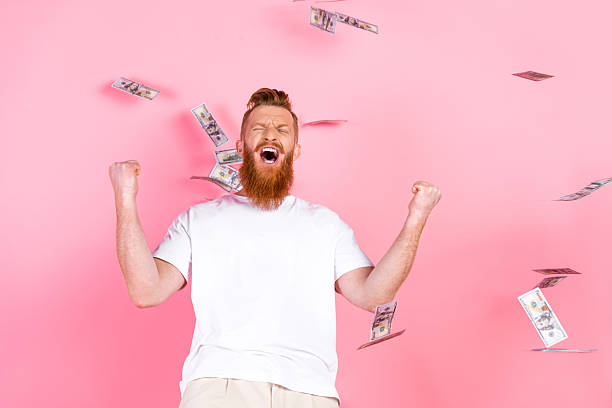 istock Excited man celebrating success with a joyful expression and money falling on a pink background, depicted in a casual white t-shirt 2218735258