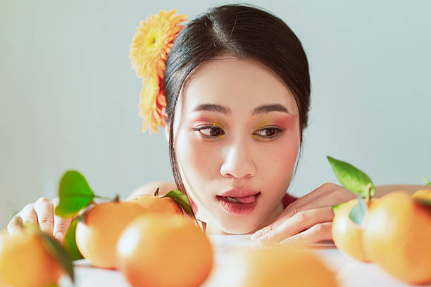 Charming scene of a young woman surrounded by vibrant mandarin oranges, exuding freshness and playful curiosity. A delightful fusion of natural citrus elements and creative expression.