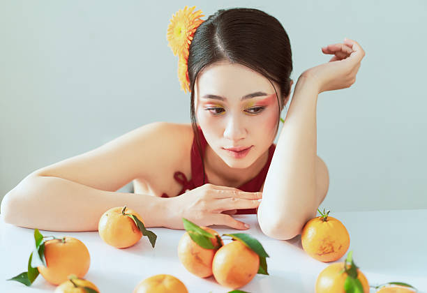 A young woman dressed stylishly, resting on a white table adorned with oranges, exuding a fresh and vibrant atmosphere.