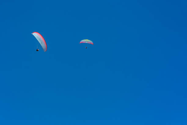 Ttwo paragliders skillfully maneuvering in opposite directions against the vibrant blue sky of Tenerife. The bright, colorful canopies of the paragliders stand out brilliantly against the clear, azure backdrop, creating a stunning visual contrast. The high-flying adventurers showcase their aerial prowess as they glide gracefully through the air, framed by the island’s breathtaking landscapes.