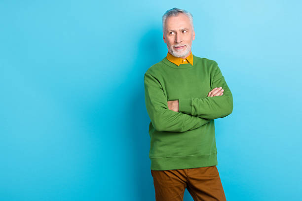 istock Photo of thoughtful man pensioner dressed green pullover arms crossed looking empty space isolated blue color background 2218744731