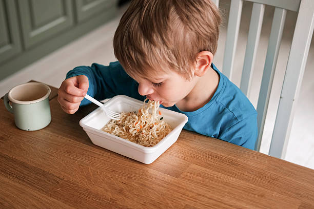istock 6 years old boy eats instant noodle from box. Child is eating spaghetti. Lunch time. A good appetite. Tasty children food. Close-up portrait. Carbs dinner. Fast food. Kid eating by himself with fork. 2218756100