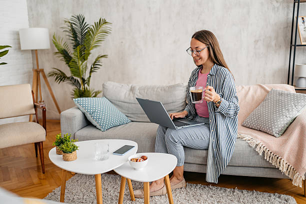 istock Young Woman Working On A Laptop And Drinking Coffee While Sitting On The Sofa At Home 2218756433