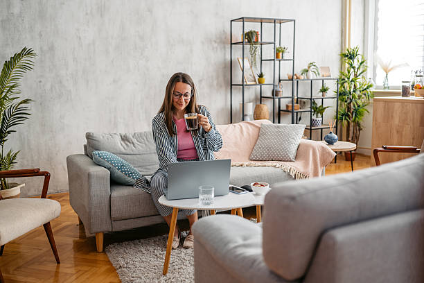 istock Young Woman Working On A Laptop And Drinking Coffee While Sitting On The Sofa At Home 2218756716