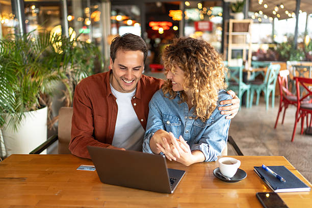 istock Happy couple using laptop and holding hands in restaurant 2218757567