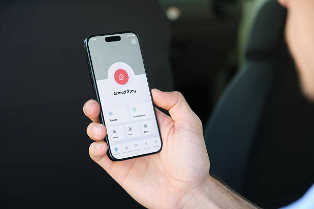 istock Man activating house alarm with smartphone app while sitting in car 2218763865