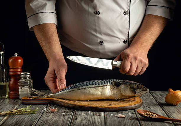 istock A chef skillfully cuts a fresh mackerel on a wooden cutting board in a cozy kitchen. Herbs and spices are arranged nearby, creating a warm culinary atmosphere 2218764536