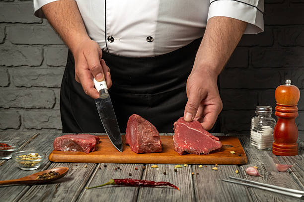 istock A chef uses a sharp knife to slice different cuts of meat placed on a wooden board. Spices and seasonings are arranged nearby, highlighting the preparation process for cooking 2218764580
