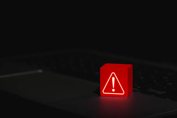 istock Cybersecurity Warning Alert Symbol. Glowing red warning triangle block with exclamation mark placed on laptop, symbolizing system threat or cyber security alert. system error, virus, spyware, malware, 2218765531