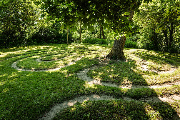Explore the serenity of a winding labyrinth under the shade of an old tree in a lush summer garden stock photo