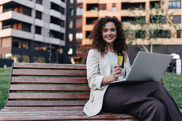 istock Confident woman on bench with laptop and card 2218779267