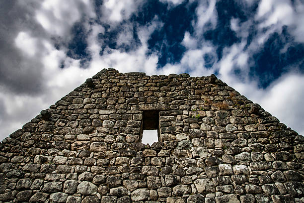 Machu Picchu, world famous archeological site in the Andes Mountains, closeup of Inca stonework, looking up stone wall, blue sky and scattered clouds above.