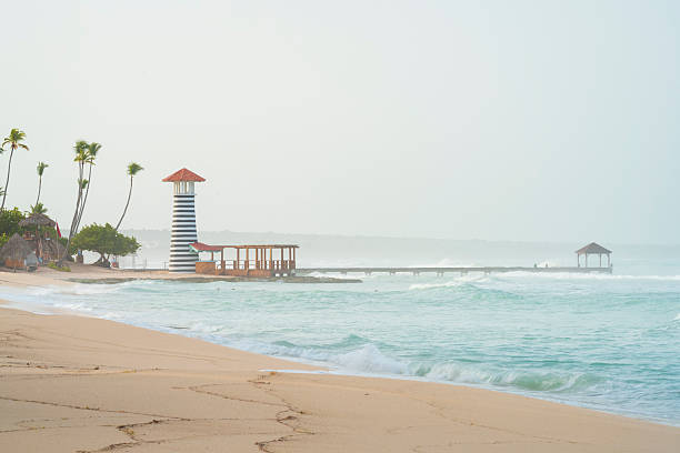 Dominican Republic beach at overcast day, Wonderful waves,rough sea and romantic lighthouse with wooden pier.