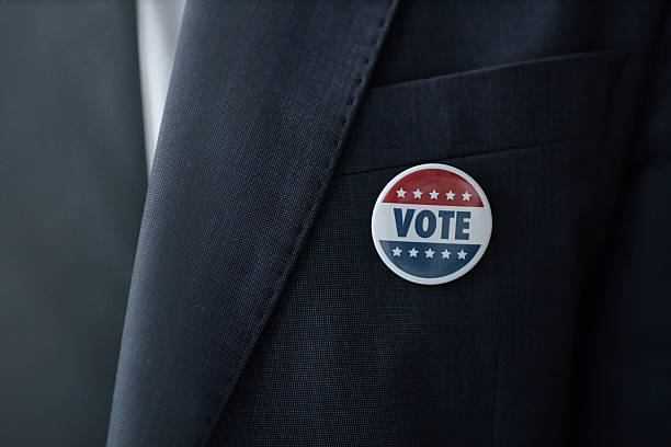 Close up on male political candidate wearing formal suit jacket with round vote badge pinned to lapel, copy space